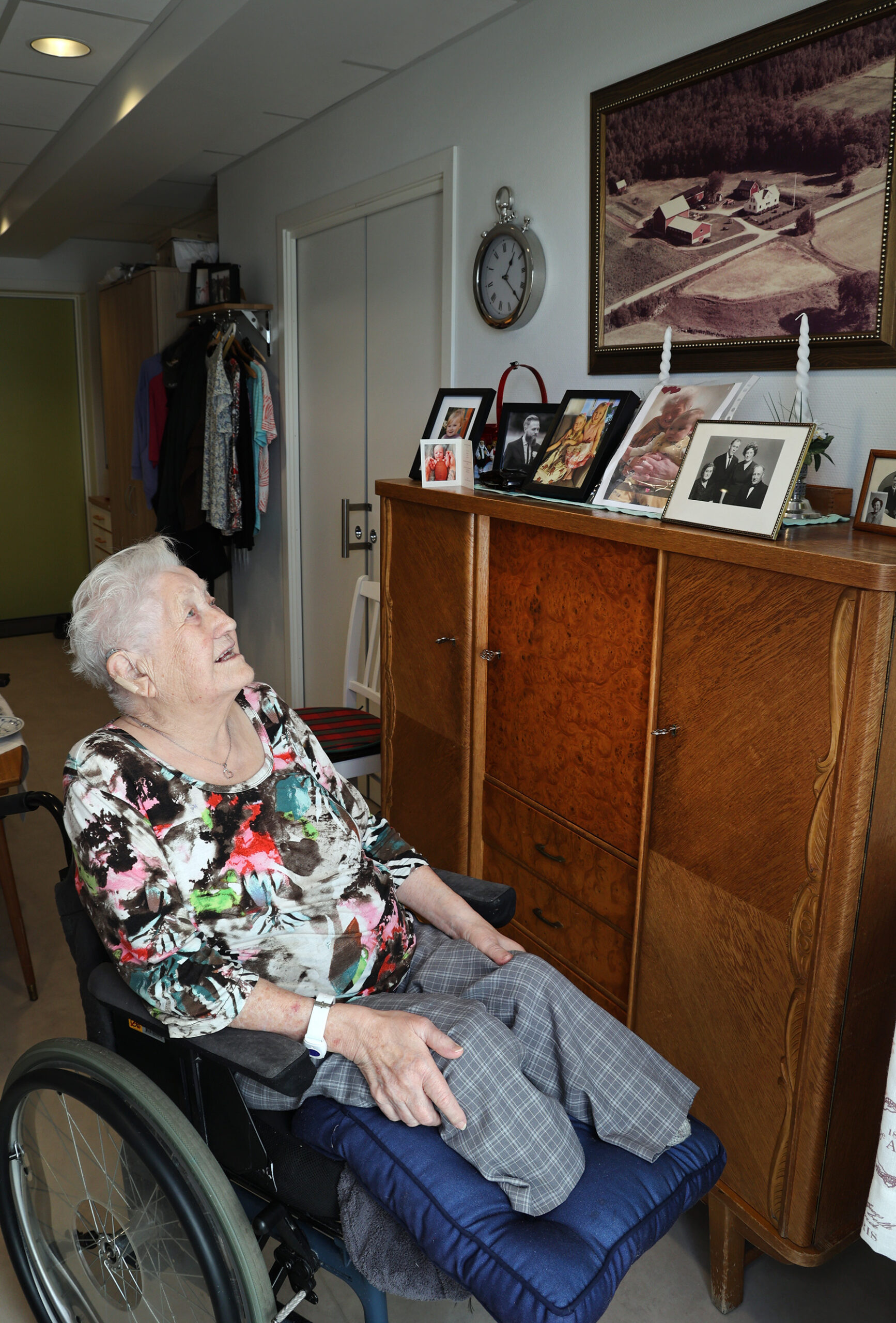 Judith foran bildet av g&aring;rden i Trefjorden, som henger i stua hennes i leiligheta.