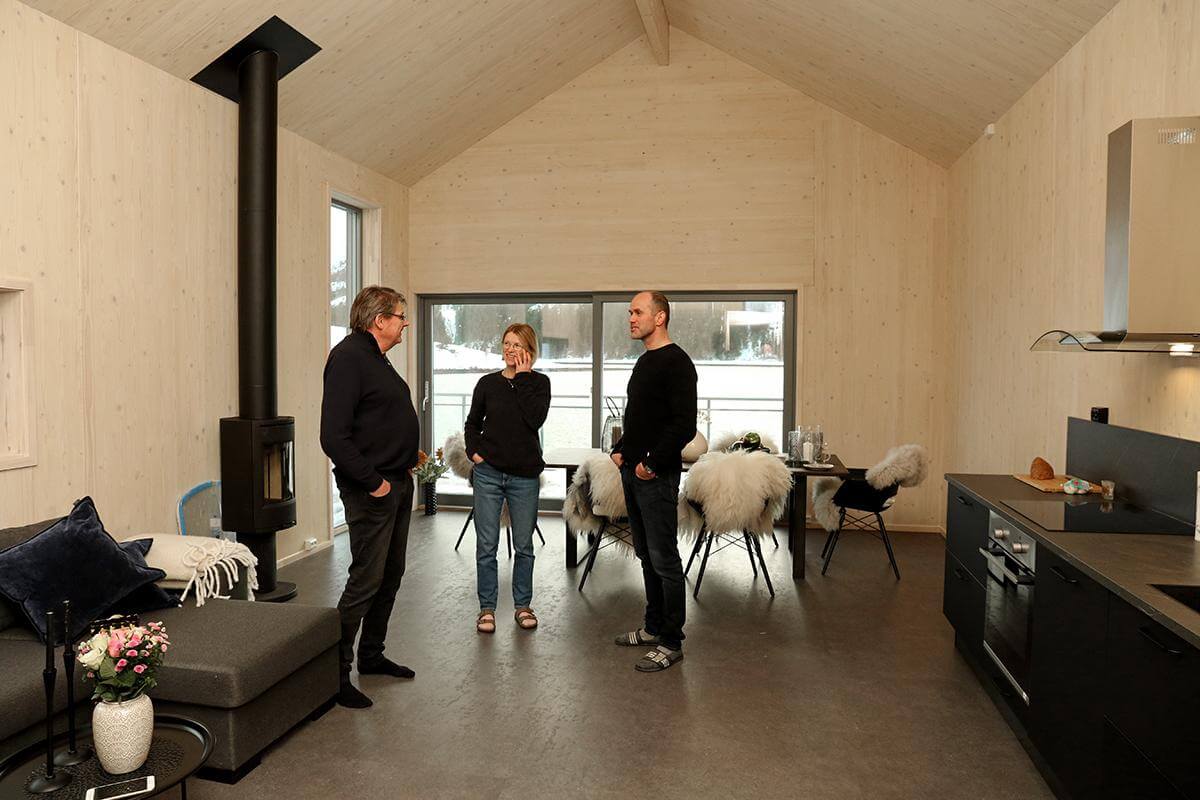 Den moderne rorbua har stue og kjøkken i samme rom, store vinduer mot fjorden og terrasse med "beina" i sjøen. Johan Sørgaard (til venstre) var innom med gaver på innflyttingsdagen til Cornelia Vikan og Harald Trettenes.