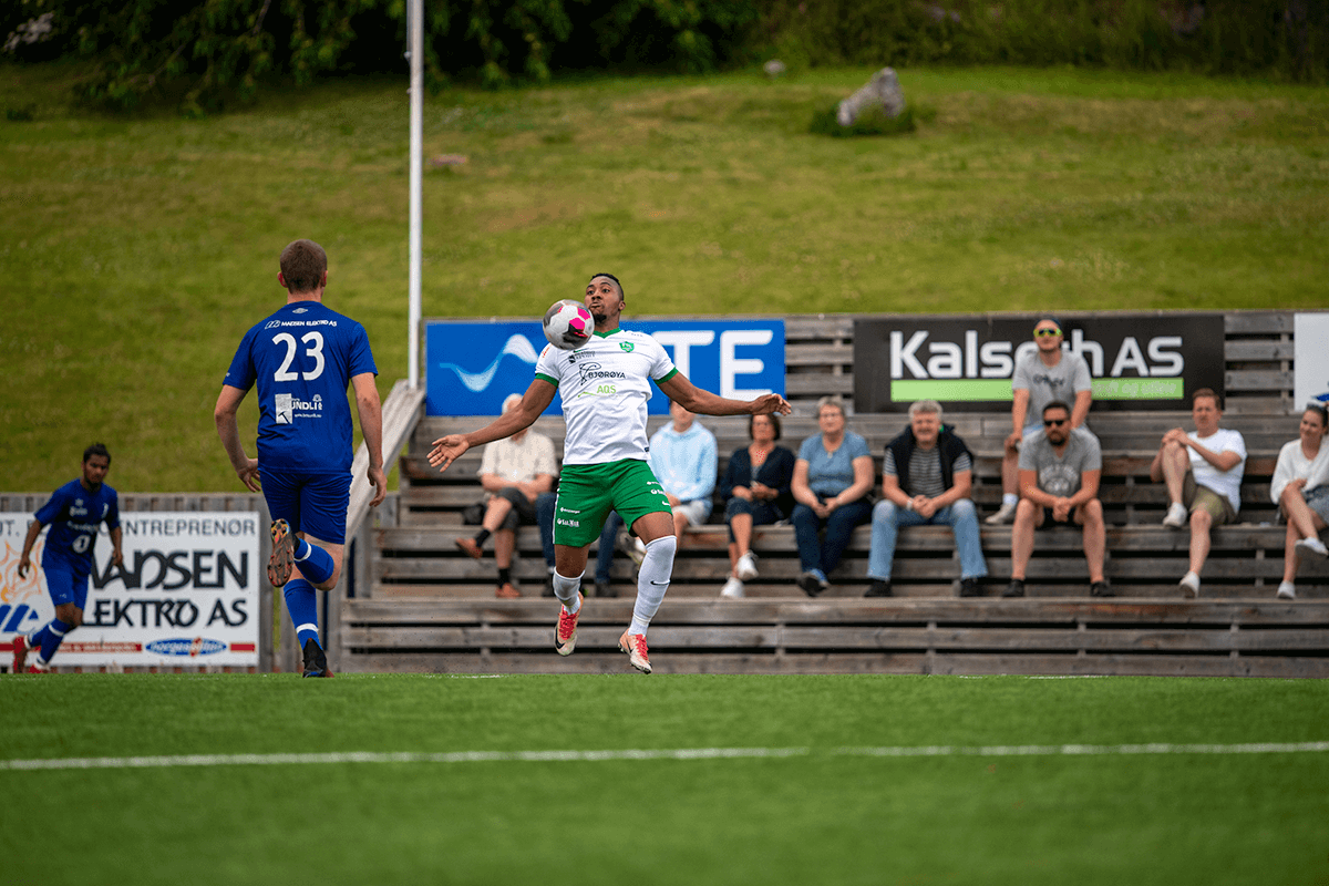 Patrck Jr. Nzobo i aksjon for Flatanger, med en stor tilskuerbenk av Flatanger-supportere i ryggen.